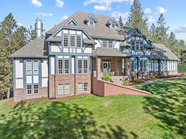 rear view of property featuring a lawn, stucco siding, roof with shingles, and brick siding