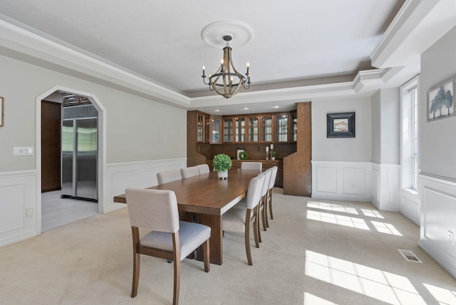 dining space with a notable chandelier, visible vents, wainscoting, and a raised ceiling