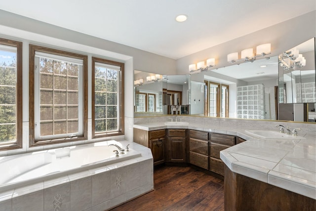 bathroom with a garden tub, recessed lighting, wood finished floors, and vanity