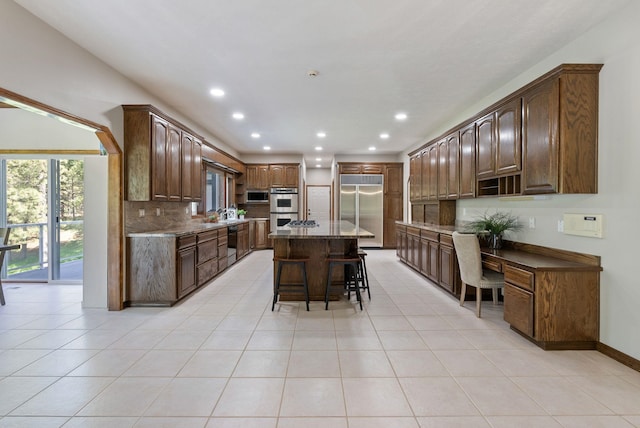 kitchen featuring light tile patterned flooring, a kitchen island, a kitchen bar, tasteful backsplash, and appliances with stainless steel finishes