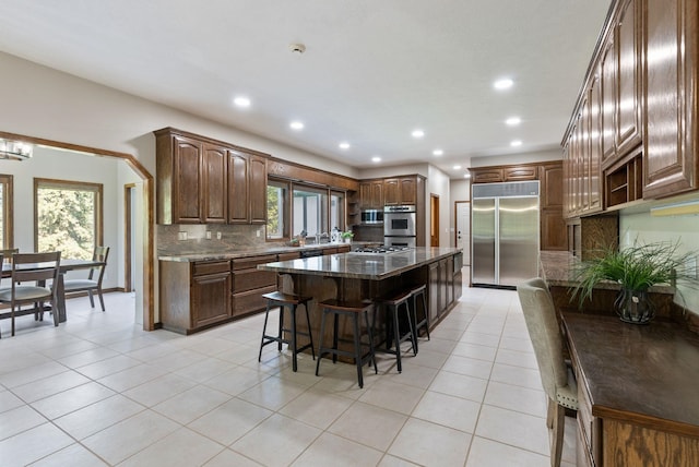 kitchen with stainless steel appliances, decorative backsplash, light tile patterned floors, a kitchen bar, and a kitchen island