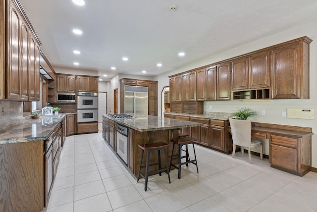 kitchen featuring light tile patterned flooring, open shelves, appliances with stainless steel finishes, built in desk, and a kitchen island