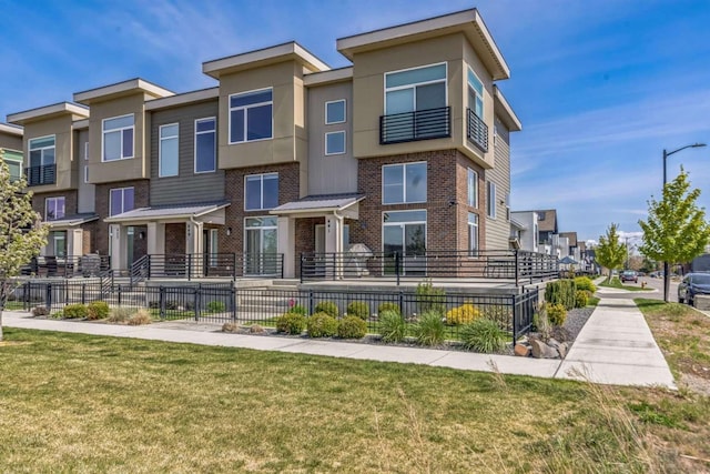 townhome / multi-family property featuring fence, a residential view, a front lawn, and brick siding
