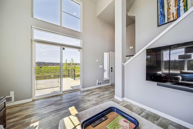 living area with visible vents, baseboards, a high ceiling, and wood finished floors