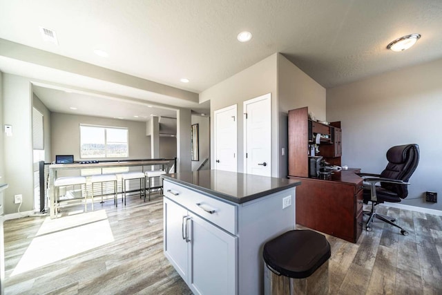 kitchen featuring visible vents, a kitchen island, dark countertops, light wood-style floors, and baseboards