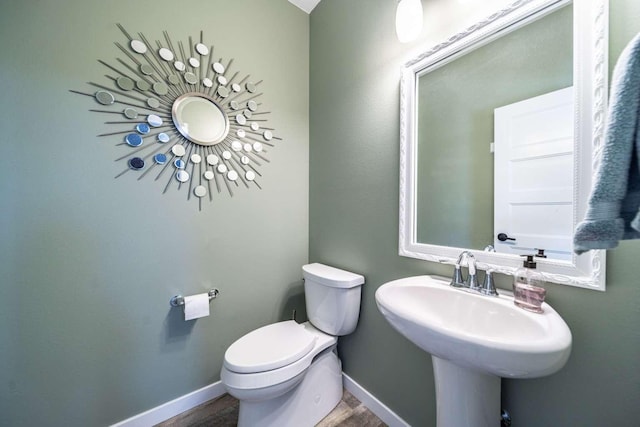 half bathroom with a sink, baseboards, toilet, and wood finished floors