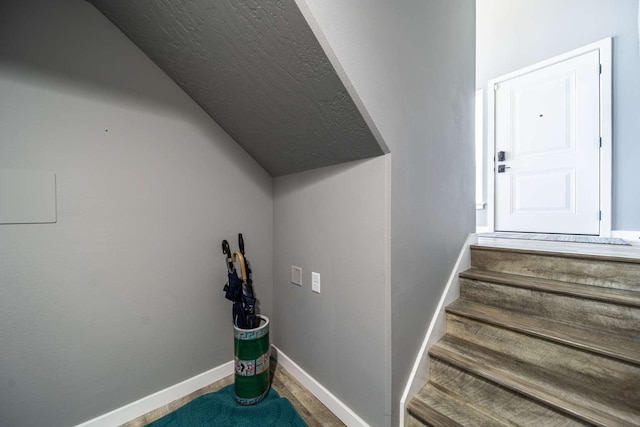 stairway featuring baseboards and lofted ceiling