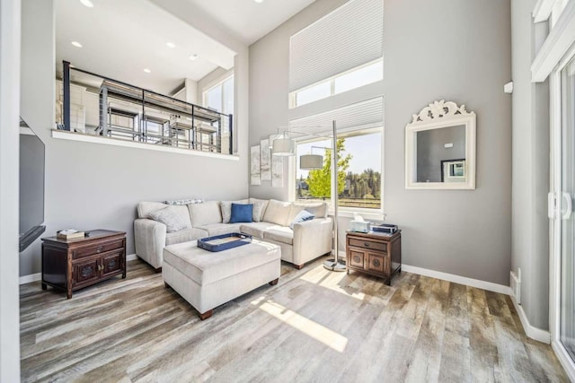 living room with wood finished floors, recessed lighting, baseboards, and a high ceiling
