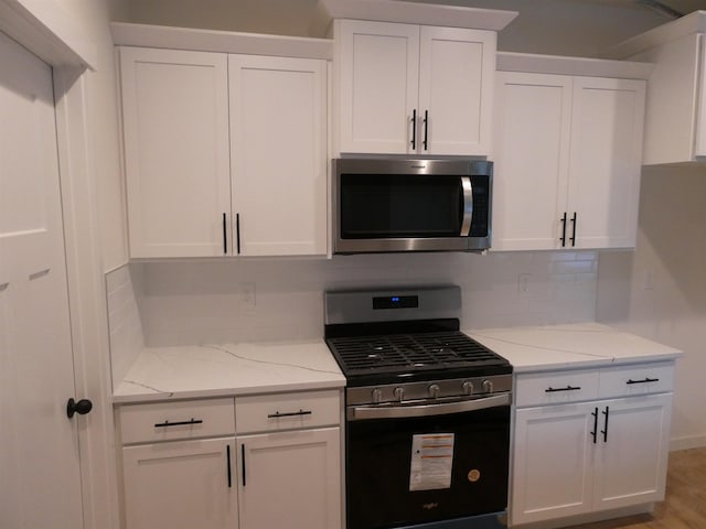 kitchen featuring light stone countertops, stainless steel appliances, white cabinetry, baseboards, and tasteful backsplash
