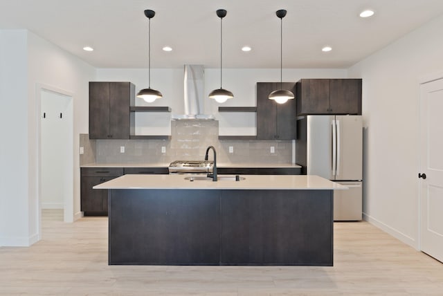 kitchen with a sink, light countertops, wall chimney exhaust hood, freestanding refrigerator, and baseboards