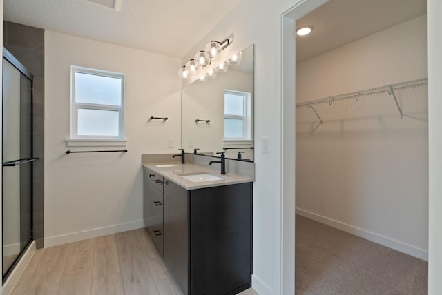 bathroom with a sink, baseboards, a shower stall, and double vanity