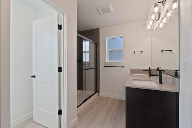 full bathroom with double vanity, wood finished floors, baseboards, a sink, and a stall shower