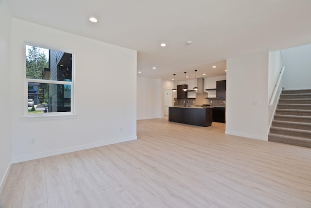 unfurnished living room with a sink, light wood-style floors, recessed lighting, baseboards, and stairway