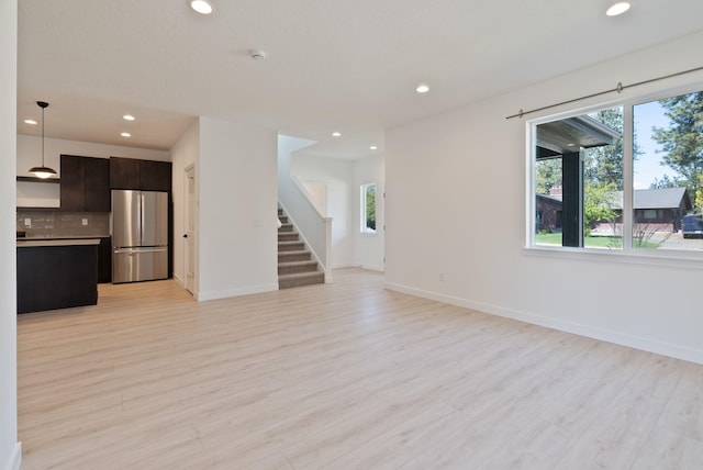 unfurnished living room with stairs, recessed lighting, a healthy amount of sunlight, and light wood-style flooring