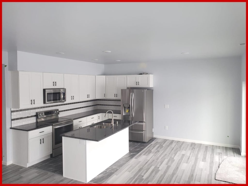 kitchen featuring dark countertops, white cabinetry, a sink, appliances with stainless steel finishes, and backsplash