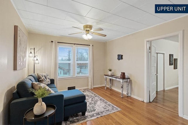 living area with light wood-type flooring, a ceiling fan, and baseboards