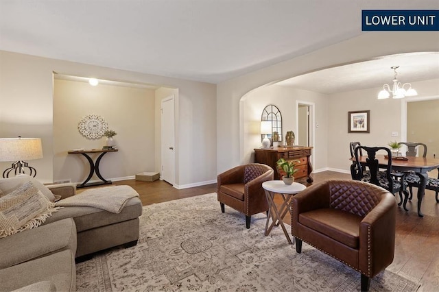 living room with arched walkways, baseboards, a notable chandelier, and wood finished floors