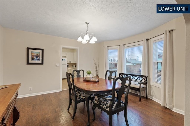 dining space with baseboards, dark wood-type flooring, a textured ceiling, and a chandelier