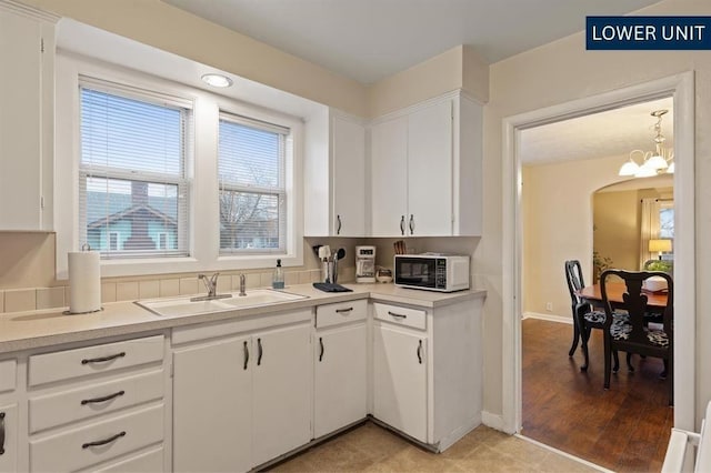 kitchen with a sink, white cabinetry, a chandelier, and light countertops