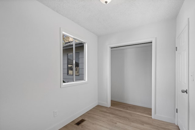 unfurnished bedroom featuring visible vents, a textured ceiling, baseboards, and light wood-style floors