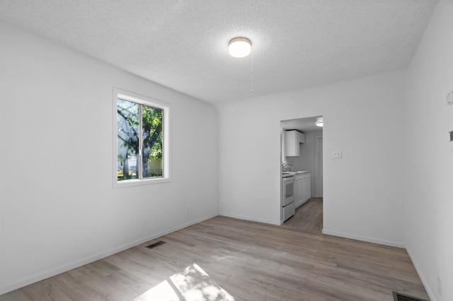 unfurnished room with baseboards, light wood-style flooring, a textured ceiling, and visible vents