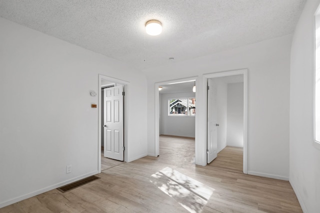 empty room featuring a textured ceiling, visible vents, baseboards, and light wood finished floors