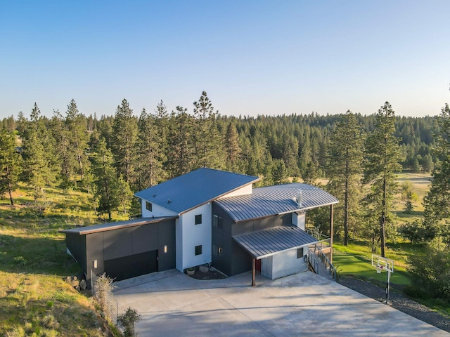 view of front of house with a standing seam roof, a view of trees, concrete driveway, and metal roof