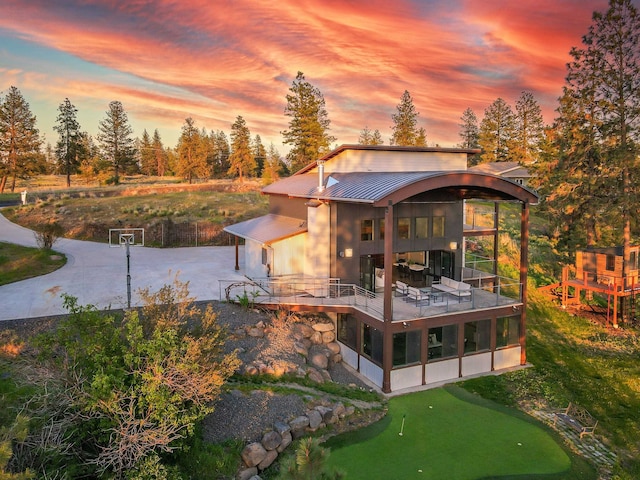 back of property at dusk featuring a sunroom, concrete driveway, a patio area, a standing seam roof, and metal roof