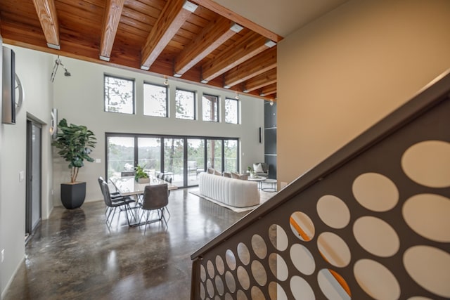 stairs with wooden ceiling, a high ceiling, beam ceiling, and finished concrete floors