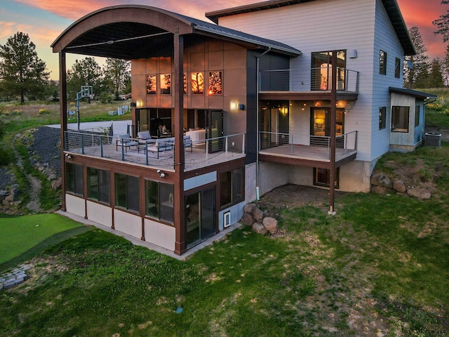 back of property at dusk with a sunroom, a lawn, central air condition unit, and a balcony