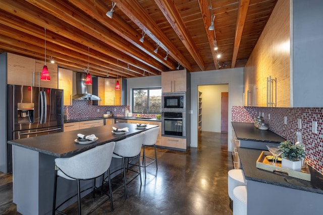 kitchen featuring wall chimney range hood, dark countertops, appliances with stainless steel finishes, track lighting, and finished concrete flooring
