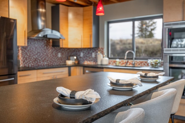 kitchen featuring wall chimney range hood, dark countertops, a breakfast bar, freestanding refrigerator, and stainless steel microwave