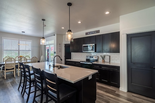 kitchen with appliances with stainless steel finishes, tasteful backsplash, a center island with sink, dark wood finished floors, and a sink