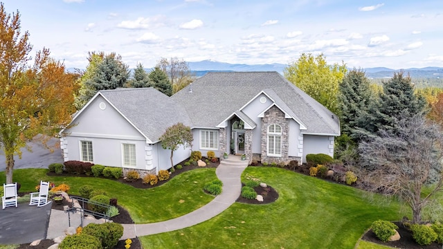 single story home featuring a shingled roof, a front lawn, a mountain view, and stone siding