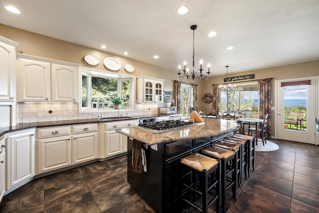 kitchen featuring an inviting chandelier, decorative backsplash, stainless steel gas cooktop, a kitchen breakfast bar, and a center island