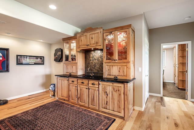 bar with baseboards, a sink, decorative backsplash, and light wood-style flooring