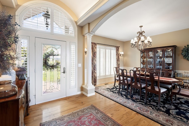 foyer entrance featuring wood-type flooring, an inviting chandelier, ornate columns, arched walkways, and a wealth of natural light