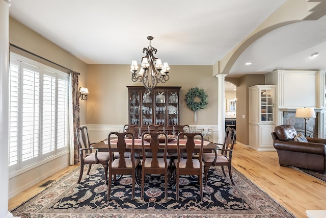 dining space with light wood-type flooring, arched walkways, and a healthy amount of sunlight