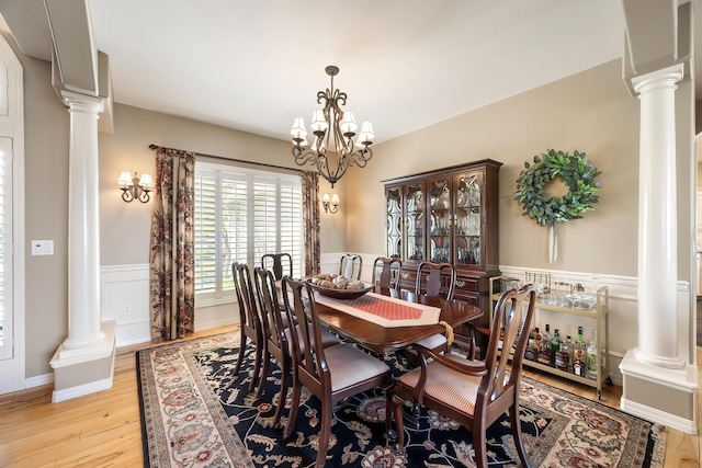 dining room with wainscoting, an inviting chandelier, decorative columns, and light wood-style flooring