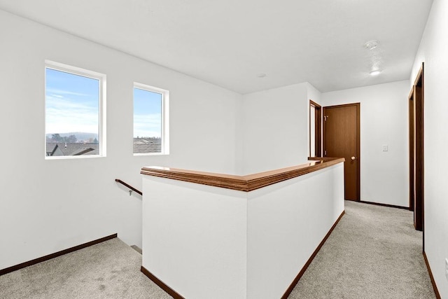 hall with light colored carpet, baseboards, and an upstairs landing