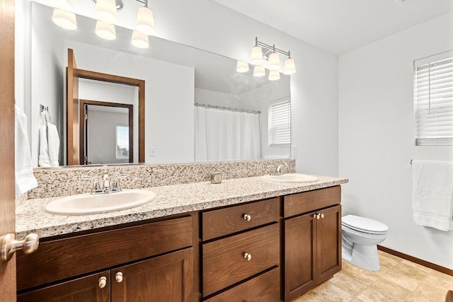 bathroom with a sink, baseboards, toilet, and double vanity