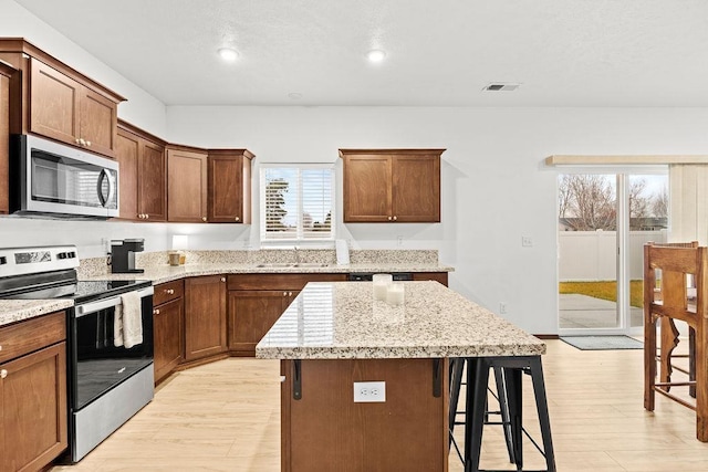 kitchen featuring appliances with stainless steel finishes, a sink, a breakfast bar area, light wood-style flooring, and a healthy amount of sunlight
