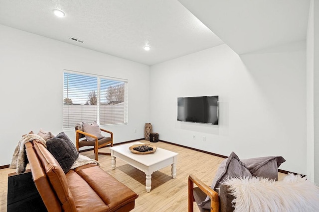 living area with baseboards, light wood finished floors, and visible vents