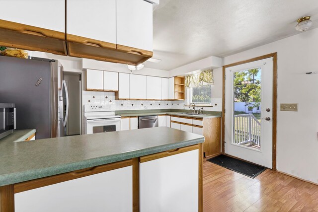 kitchen featuring a peninsula, light wood-style floors, white cabinets, a sink, and stainless steel appliances