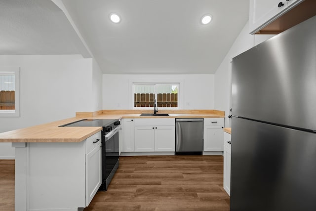 kitchen featuring butcher block counters, a peninsula, dark wood-style floors, a sink, and stainless steel appliances