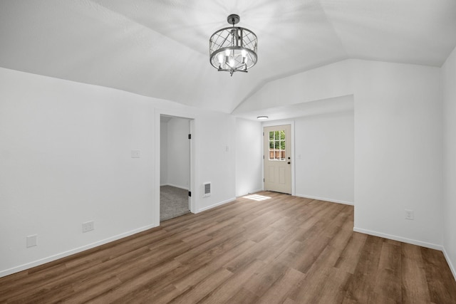 empty room featuring visible vents, wood finished floors, baseboards, a notable chandelier, and lofted ceiling