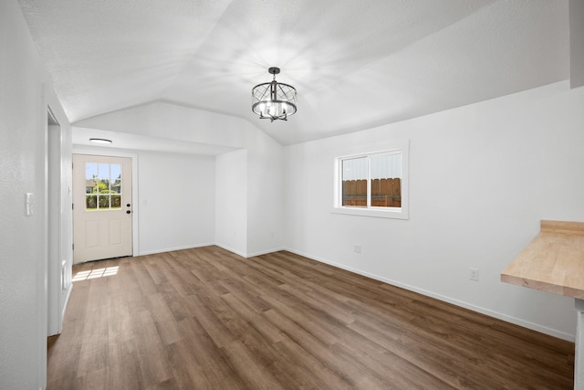 interior space with a chandelier, baseboards, vaulted ceiling, and wood finished floors
