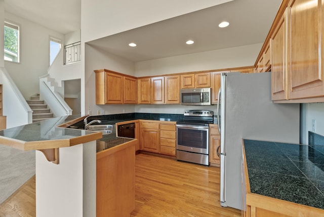 kitchen with appliances with stainless steel finishes, a breakfast bar, light wood-style floors, tile counters, and a peninsula