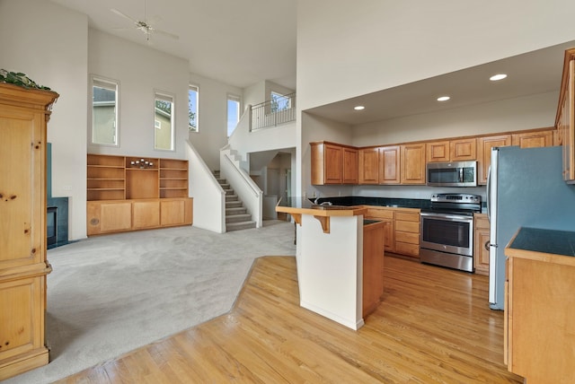 kitchen featuring a towering ceiling, a peninsula, open floor plan, a kitchen bar, and stainless steel appliances
