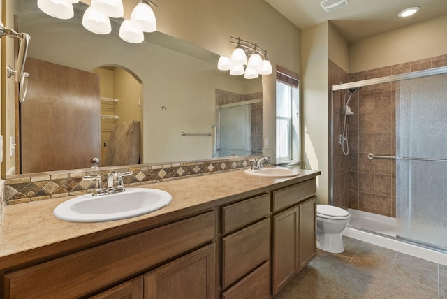 bathroom featuring double vanity, a sink, a stall shower, and toilet